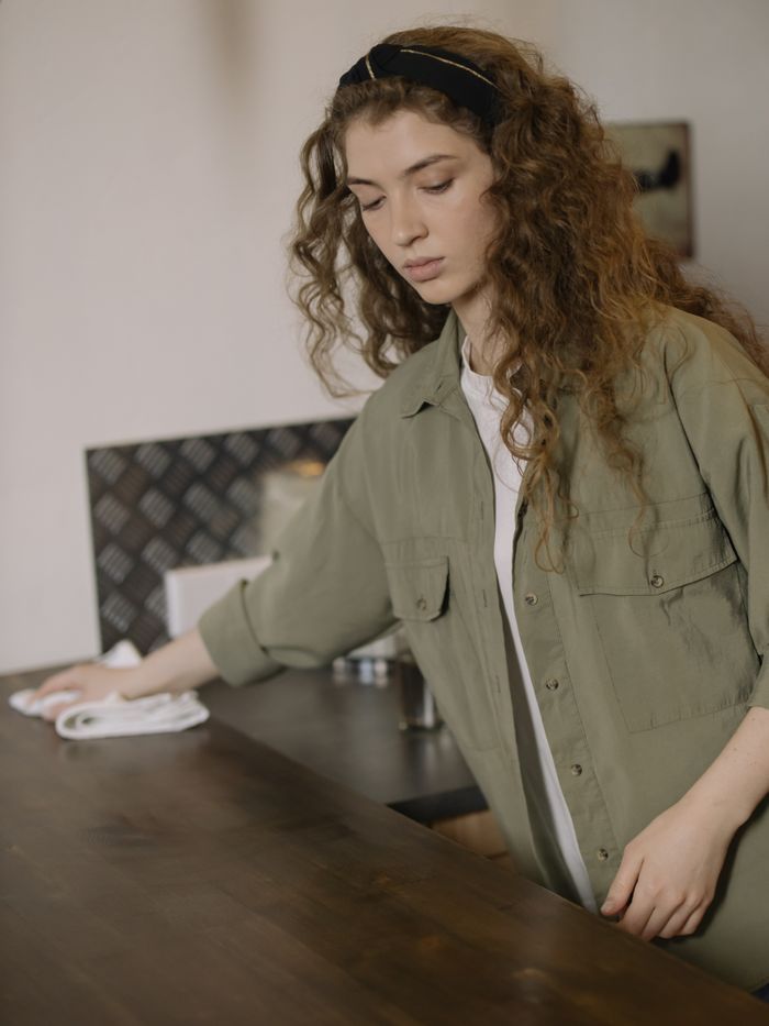 about-img-01 A young woman with curly hair cleaning a kitchen counter at home, creating a cozy and tidy environment.