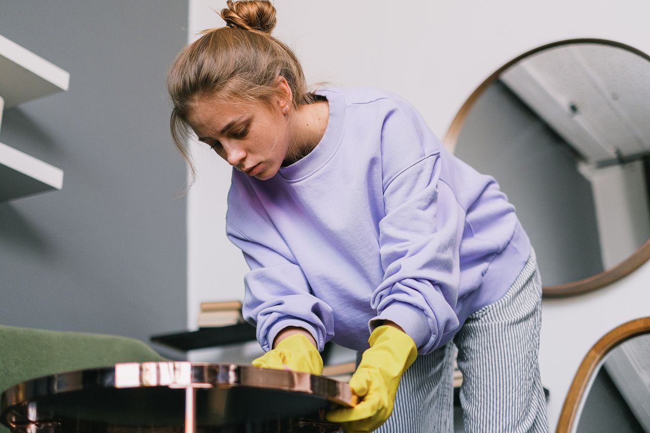 gallery-01 From below of young female in casual clothes and latex gloves standing and wiping table against mirrors in light room in daytime